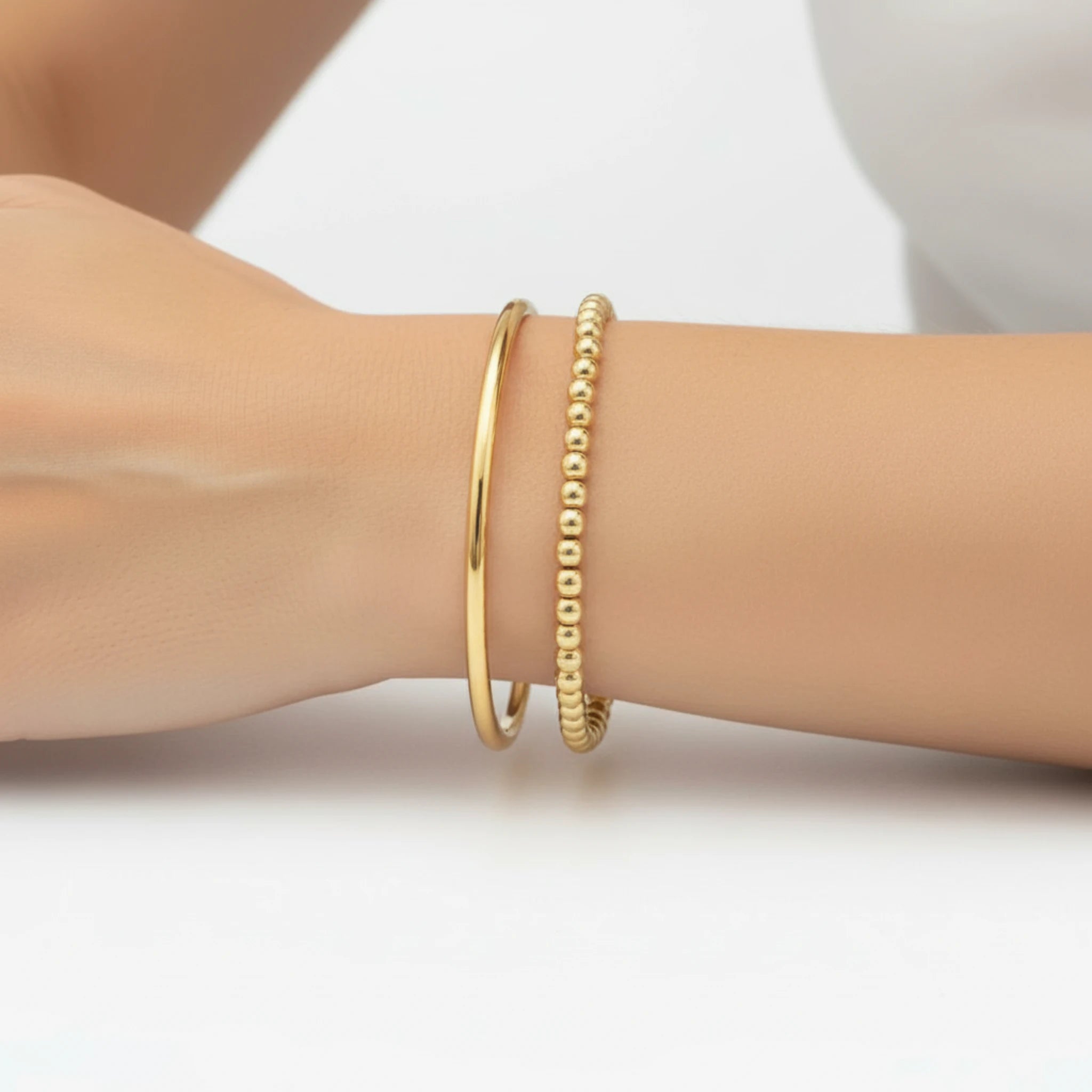 Gold bracelets on a wrist against a white background