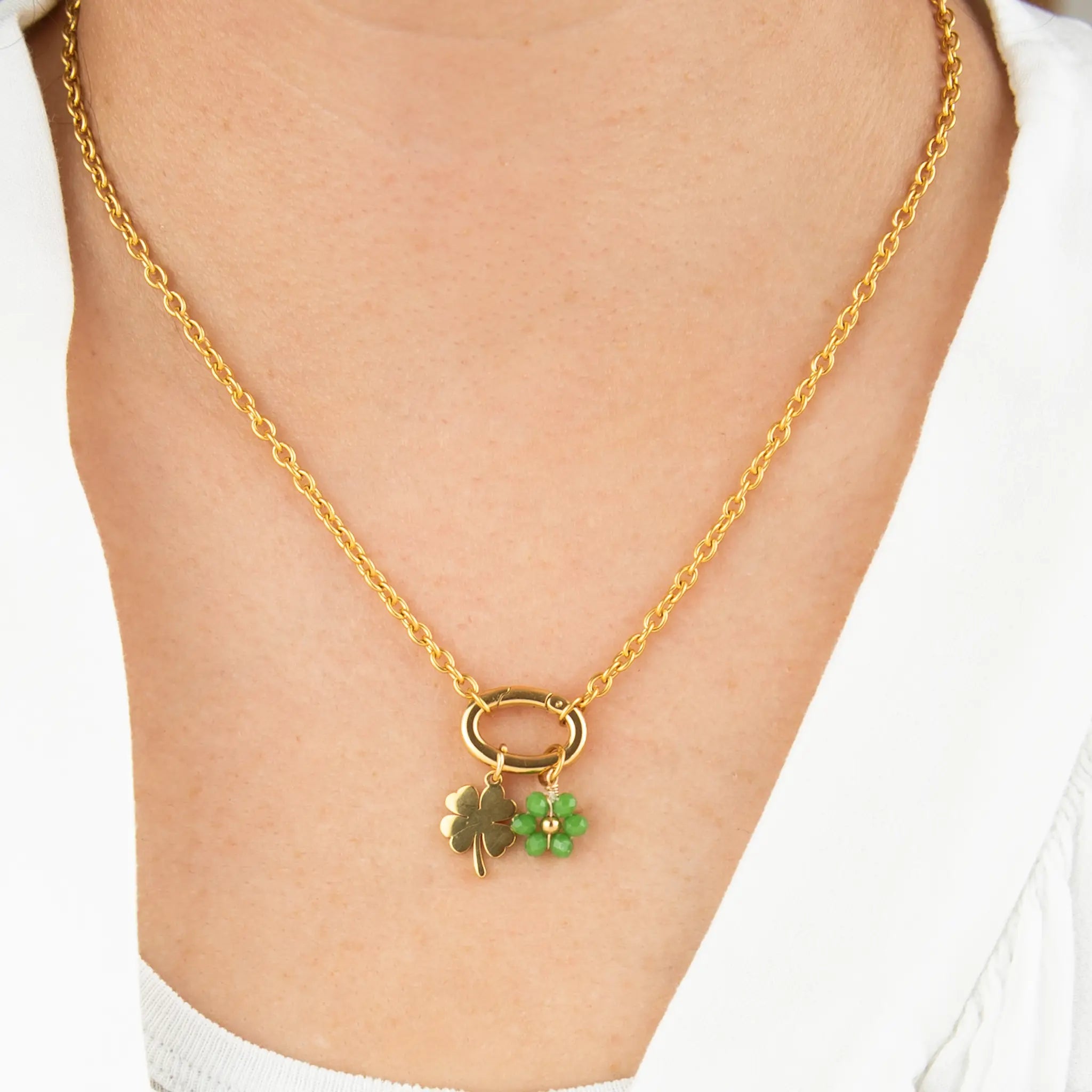 gold necklace with a clover and green flower charm on a person wearing a white shirt