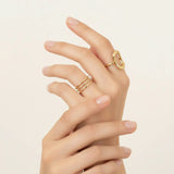 Hand wearing two gold rings on a beige background