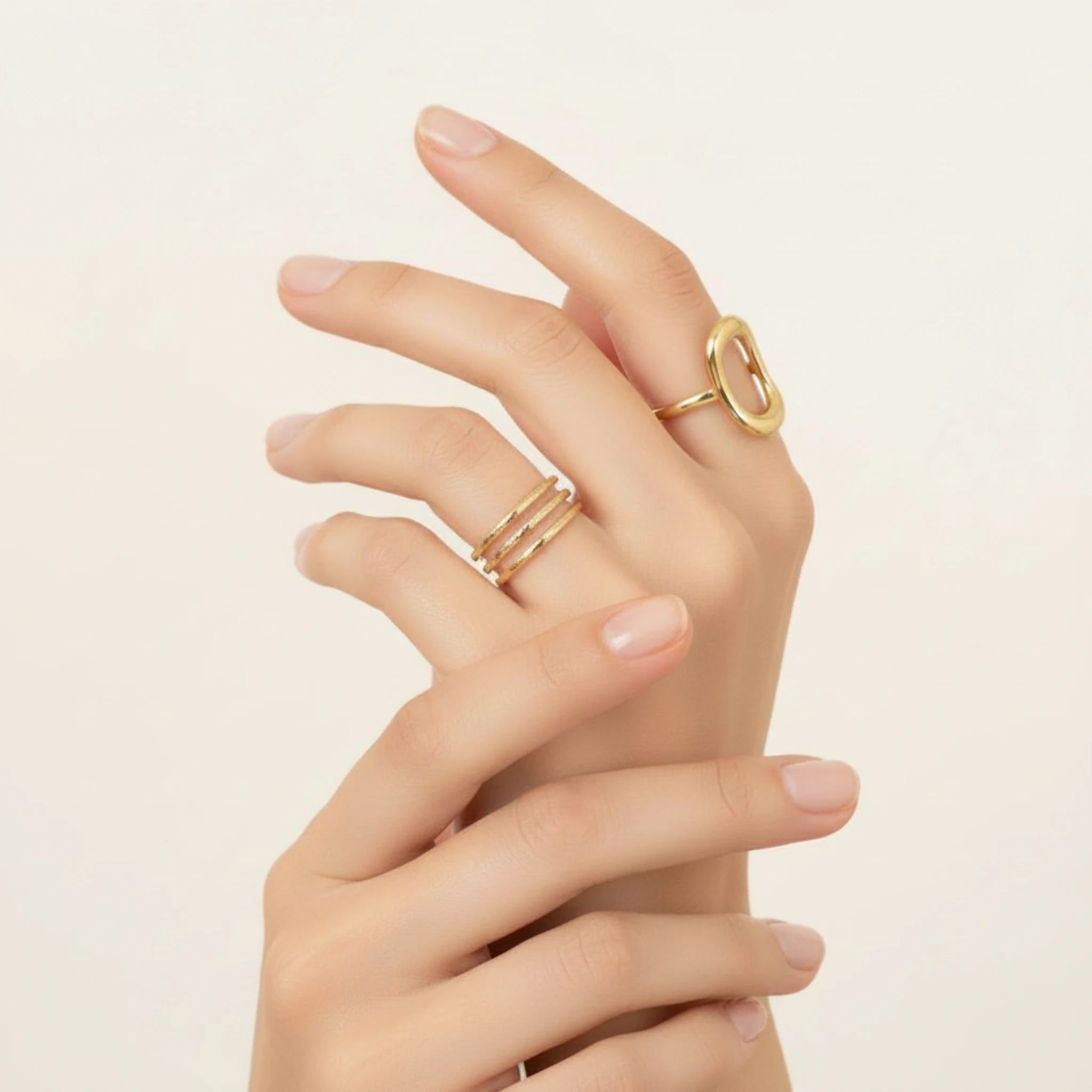 Hand wearing two gold rings on a beige background