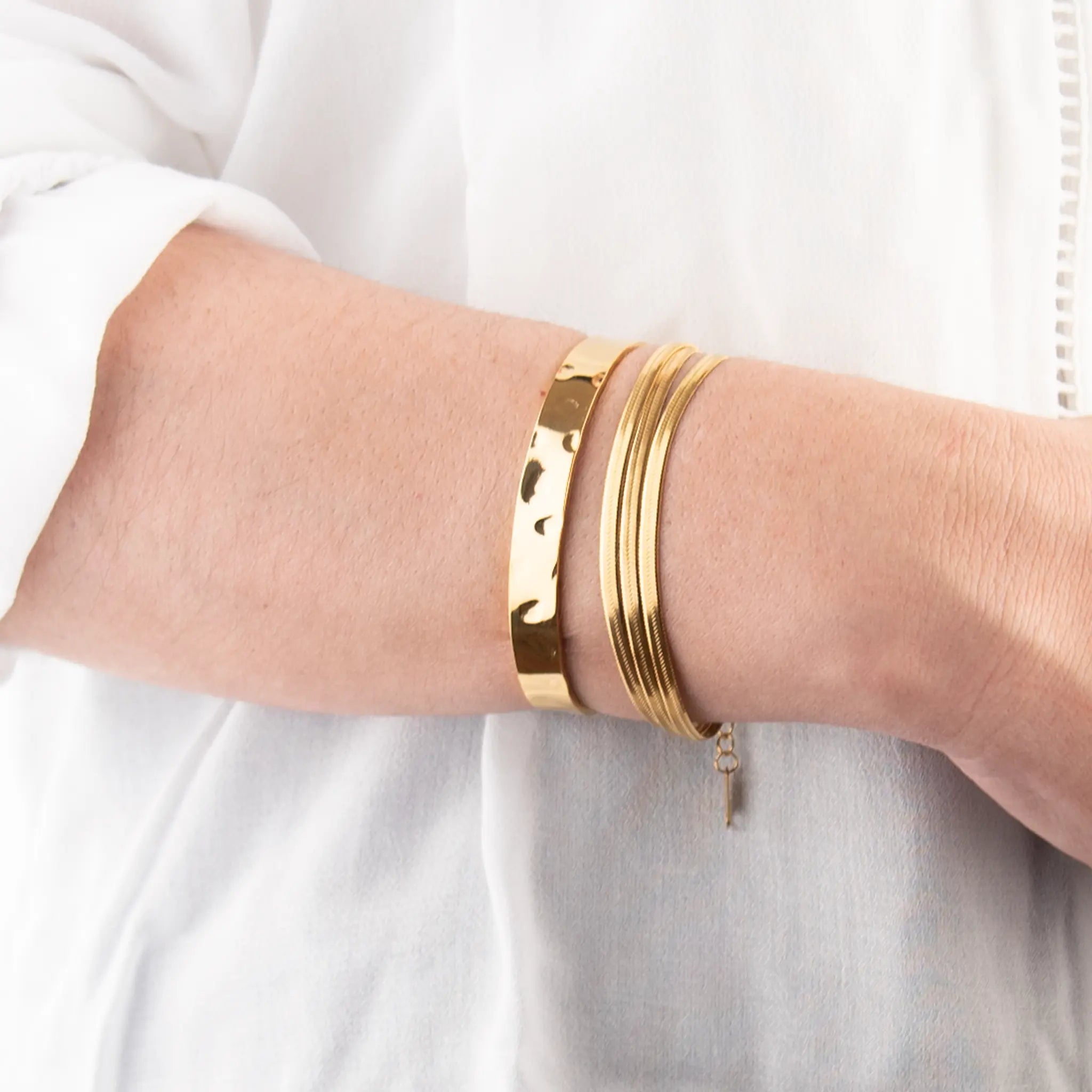 Golden bracelets on a person's wrist against a white background