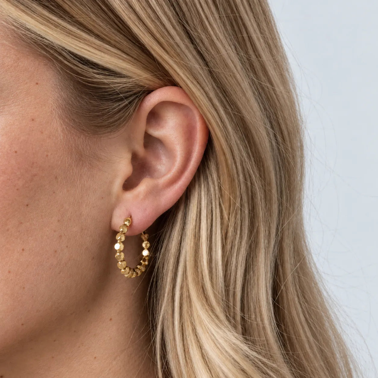 Close-up of a woman wearing gold beaded texture hoop earrings with a neutral background