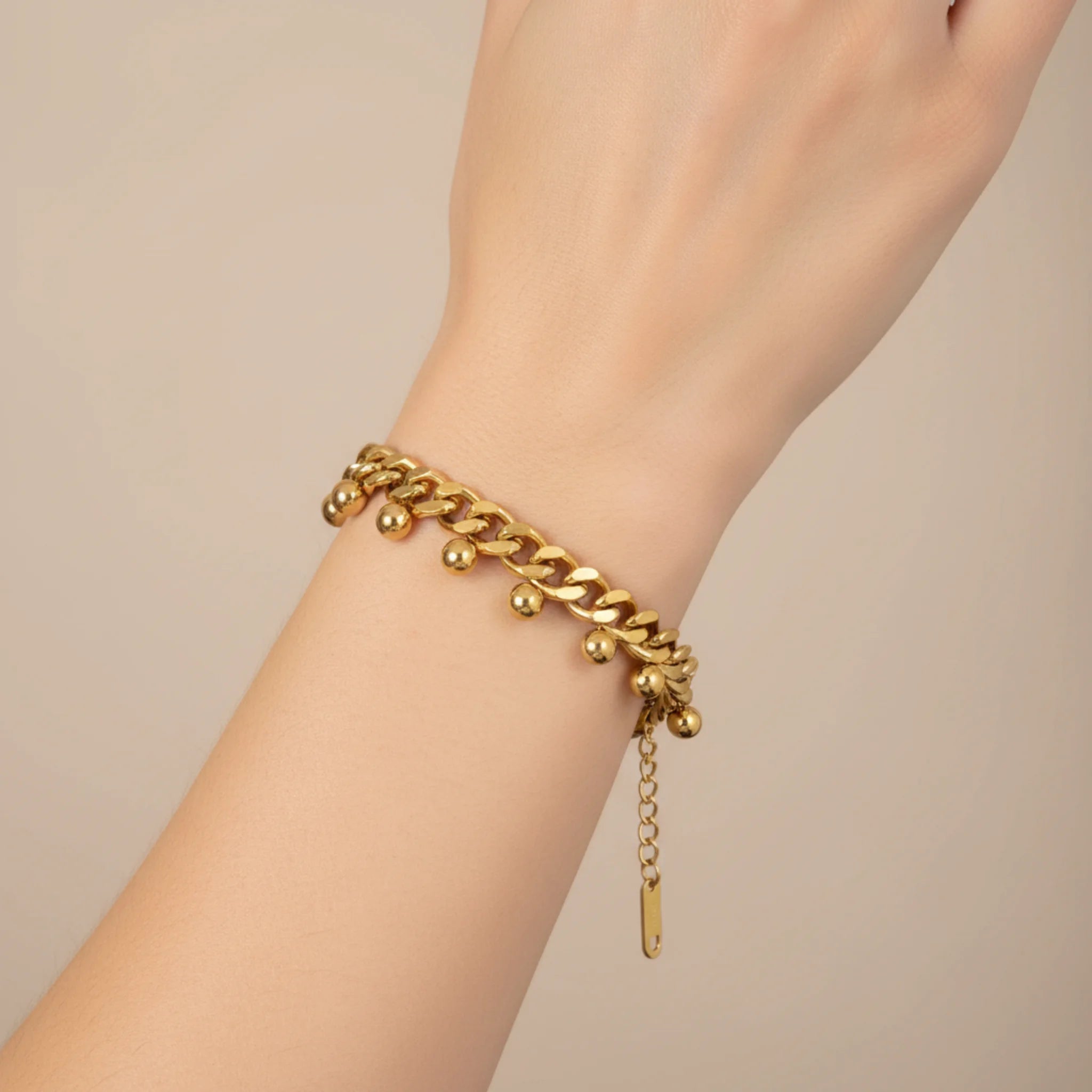 Gold chain bracelet with drops on a wrist against a beige background