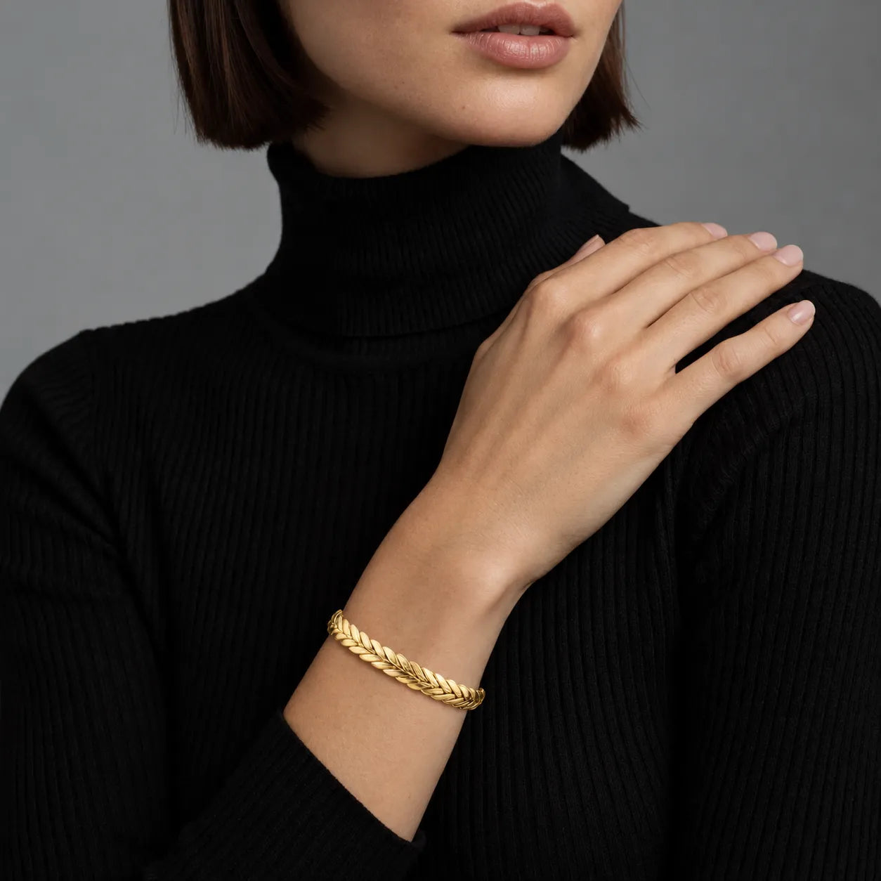 Woman wearing a gold braided cuff bracelet on a plain background