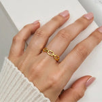 Hand wearing a gold chain link ring on a neutral background