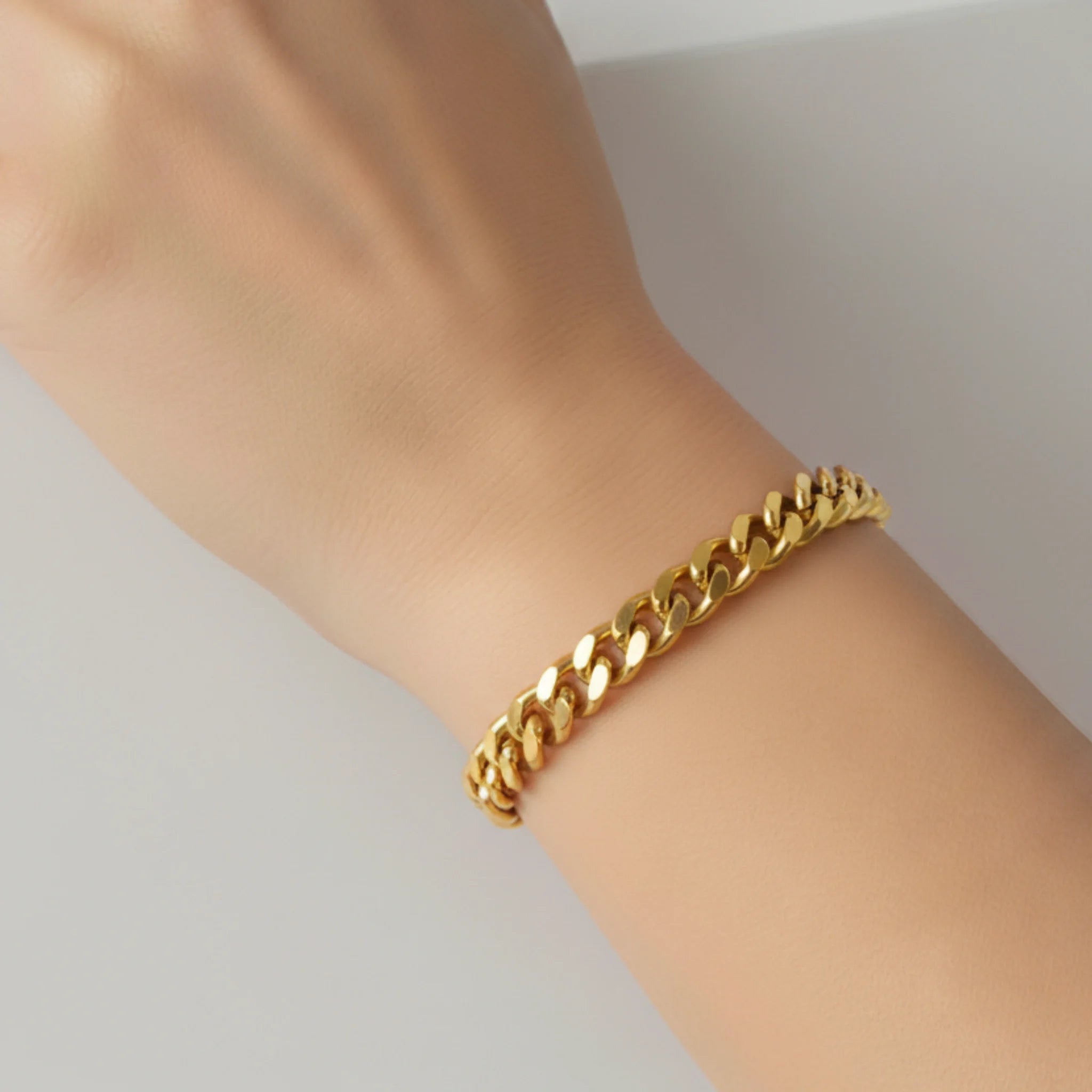 Gold chain bracelet on a wrist against a neutral background