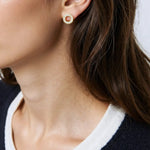Close-up of a person wearing gold crystal circle studs earrings