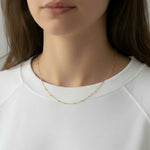A woman wearing a gold dainty beaded choker necklace against a plain background