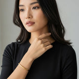 Woman wearing a black top with a gold essential cuff bracelet on a neutral background