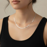 a woman wearing a fine silver herringbone necklace and a black top