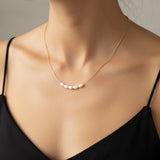 Gold necklace with pearls worn by a person against a neutral background
