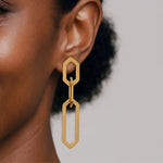 Gold geometric link drop earring worn by a person with a neutral background