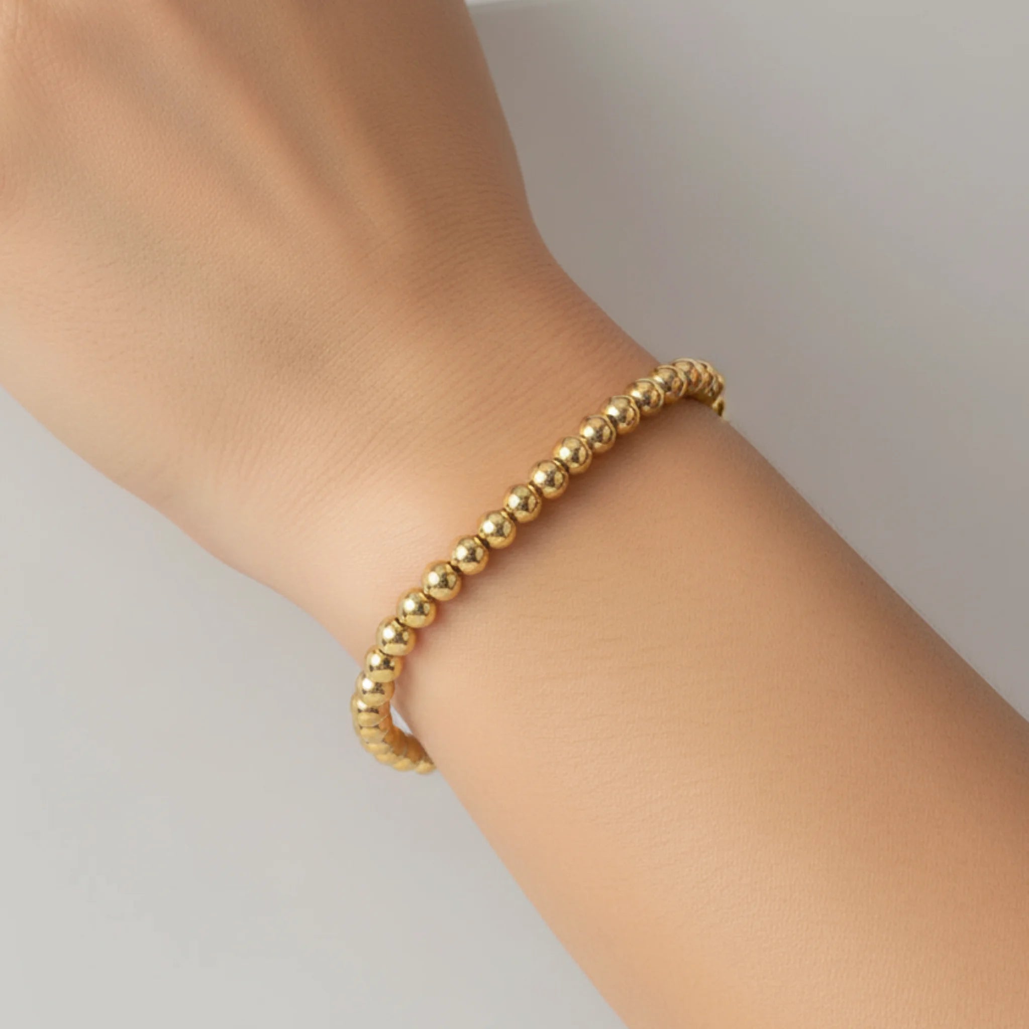 Gold beaded bracelet on a wrist against a neutral background