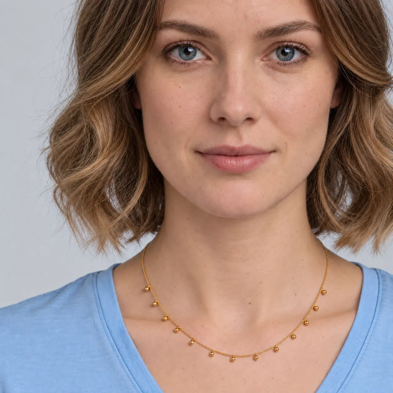 Woman wearing a gold beaded drop necklace with a blue shirt