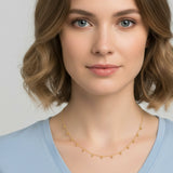 Woman wearing a gold beaded drop necklace with a blue shirt