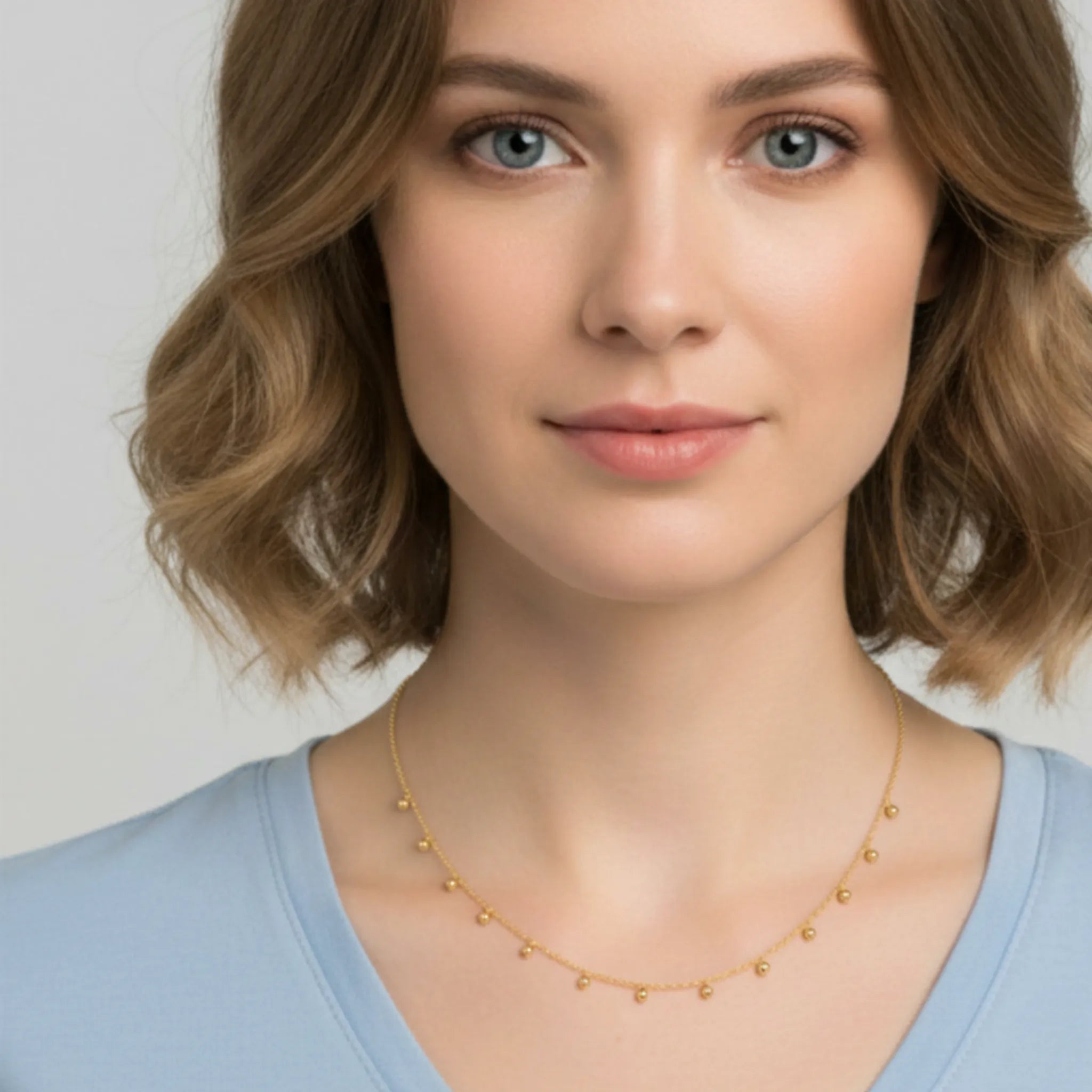 Woman wearing a gold beaded drop necklace with a blue shirt