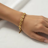 Gold cowrie shell bracelet on a wrist against a white background