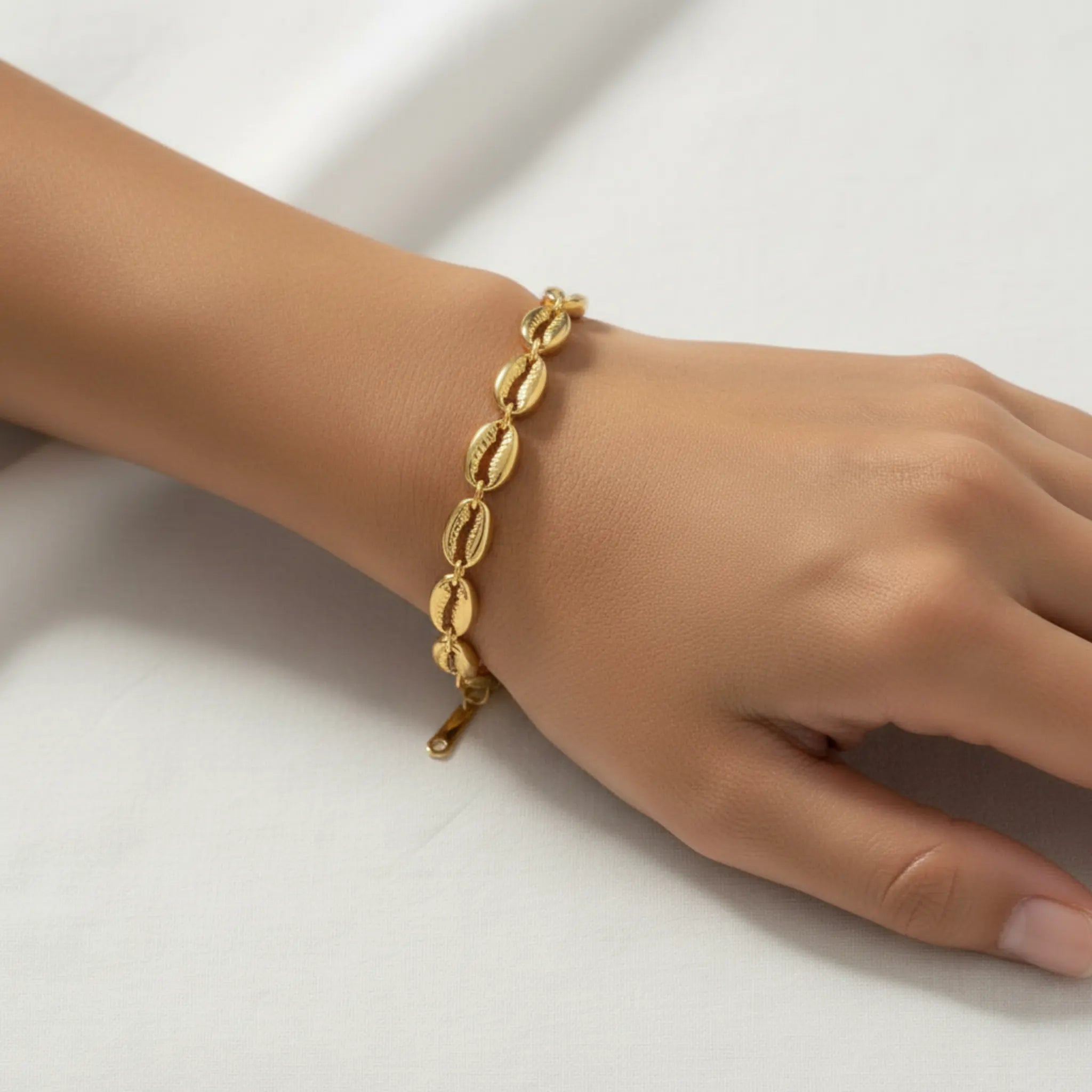 Gold cowrie shell bracelet on a wrist against a white background