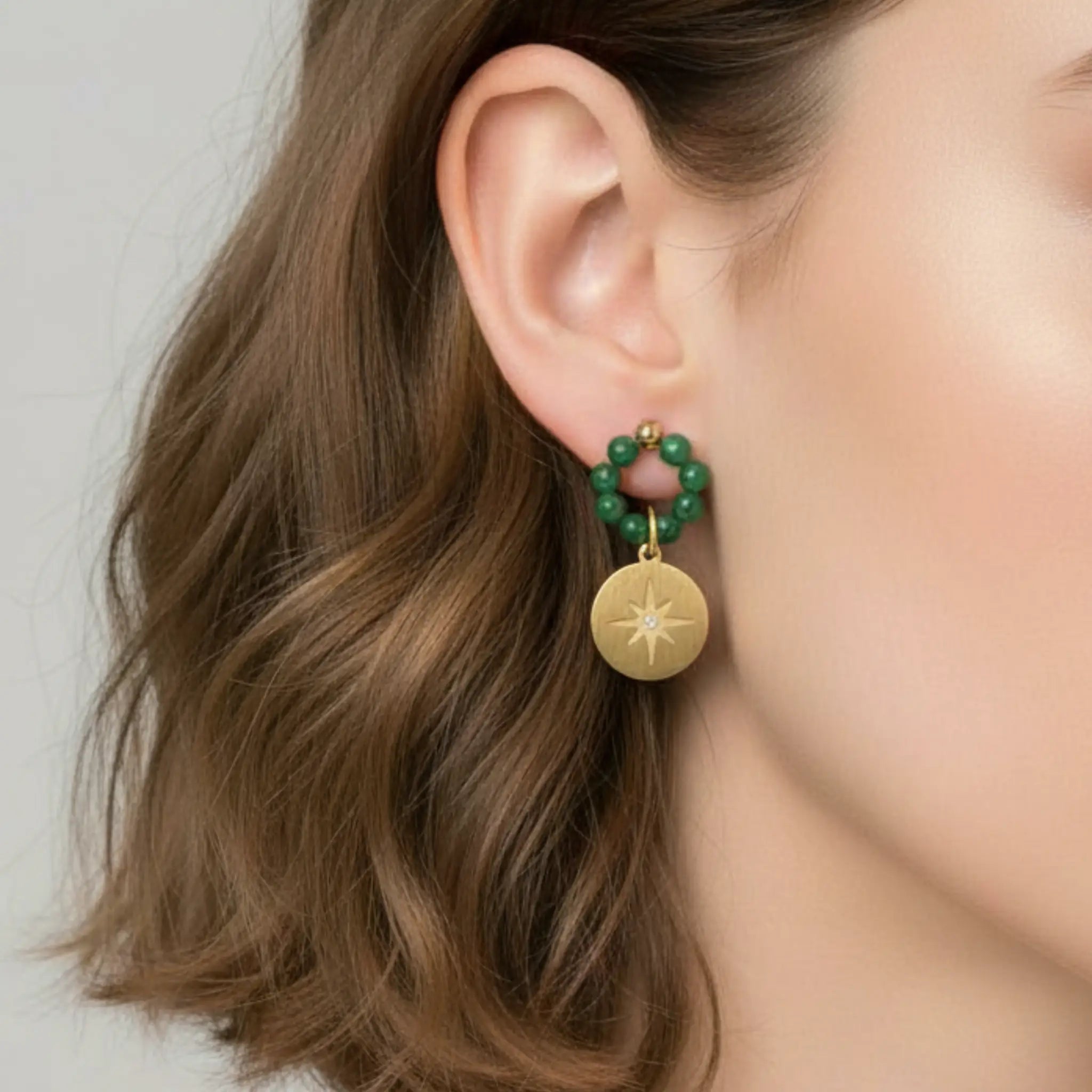 Gold earring with green beads worn by a person against a neutral background