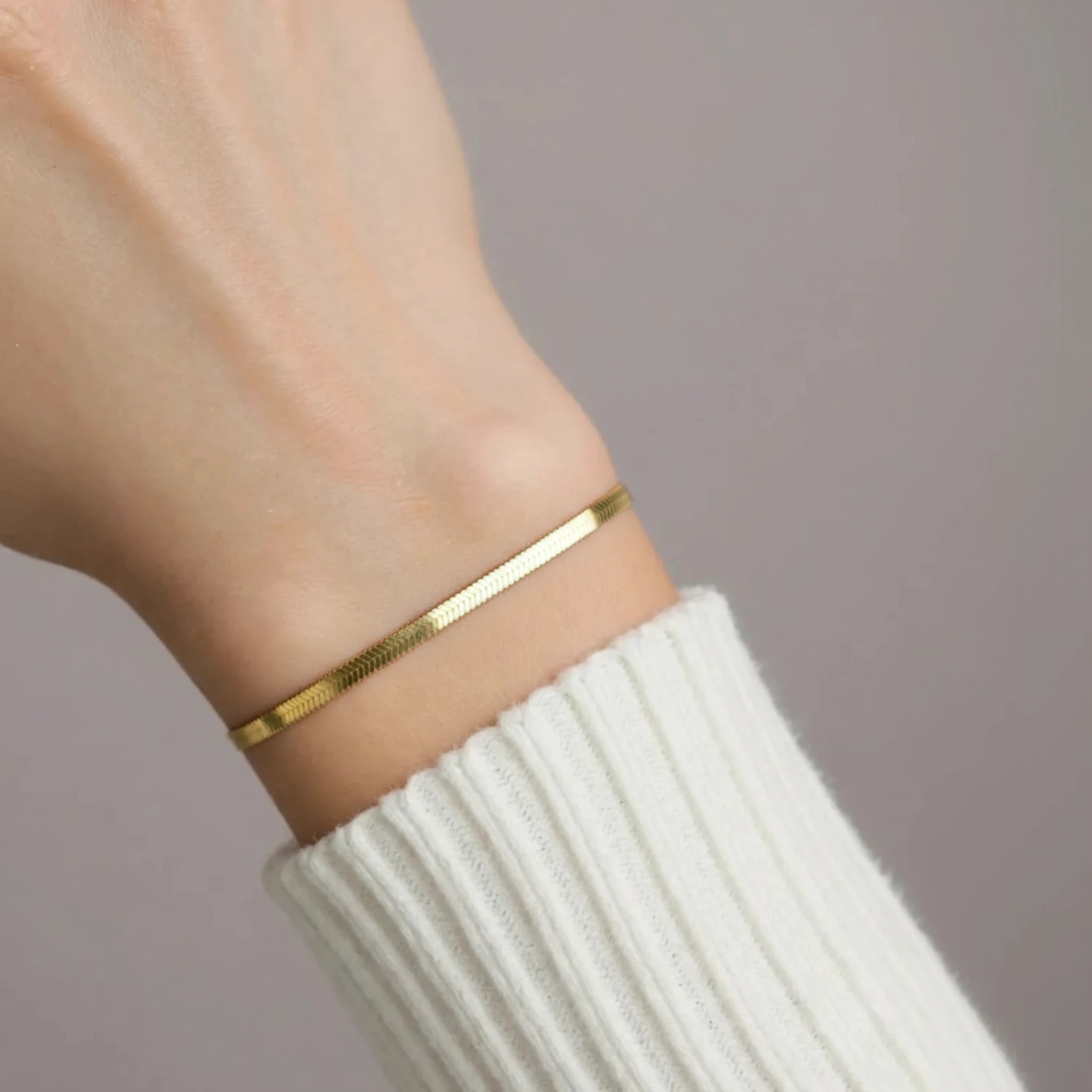 Gold herringbone bracelet on a wrist with a neutral background