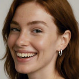 Close-up of a woman wearing a silver octagon hoop earring with a plain background