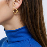 Close-up of a person wearing a gold organic circle stud earring with a blue sweater