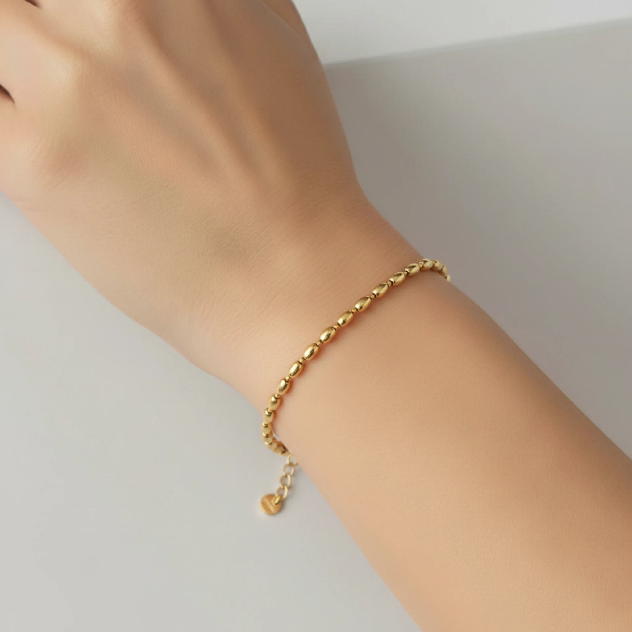 Gold oval bead bracelet on a wrist against a neutral background