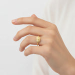 Gold sunburst signet ring on a woman's finger against a plain background