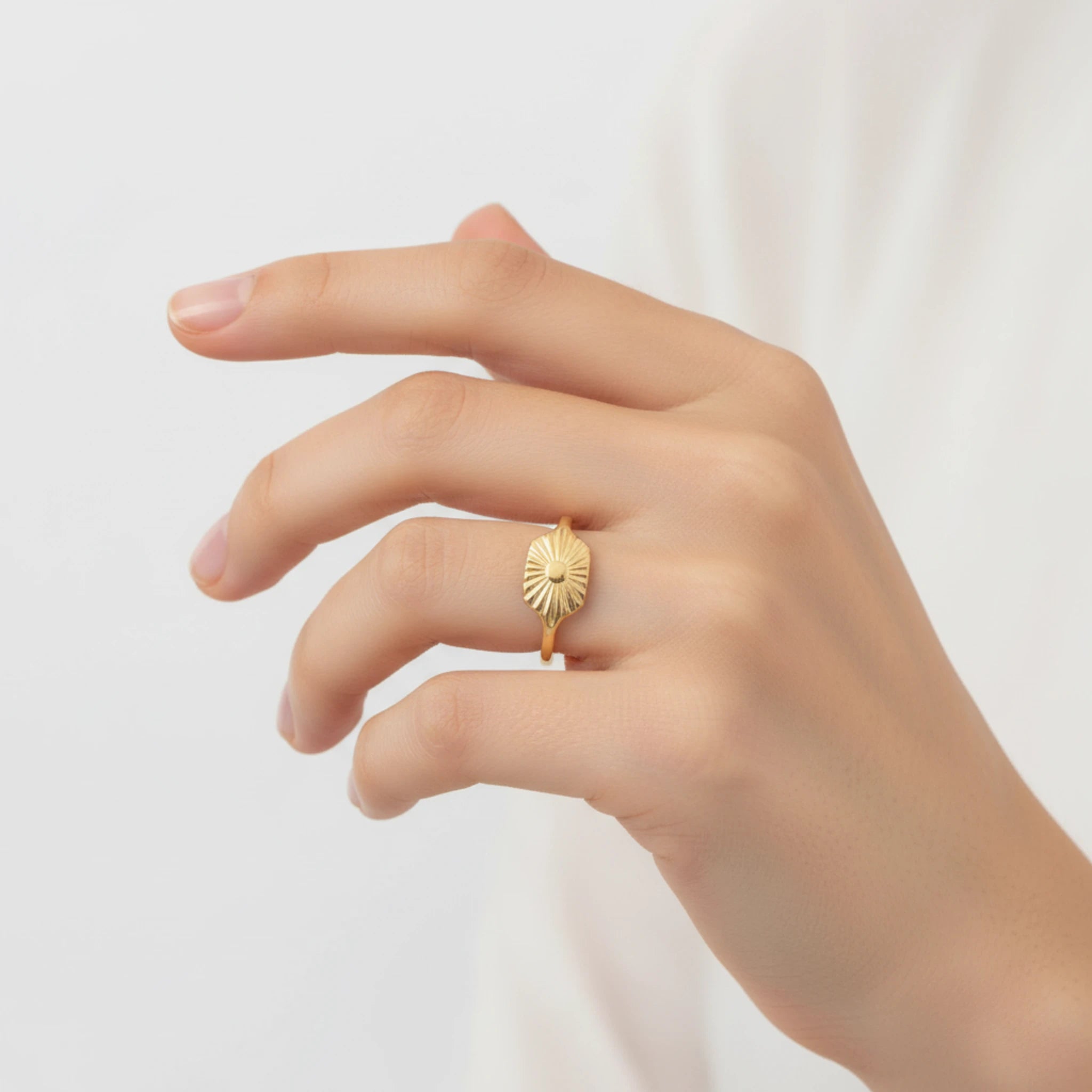 Gold sunburst signet ring on a woman's finger against a plain background