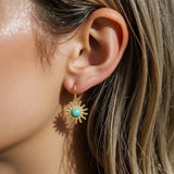 Close-up of an ear wearing a gold earring with a turquoise stone.