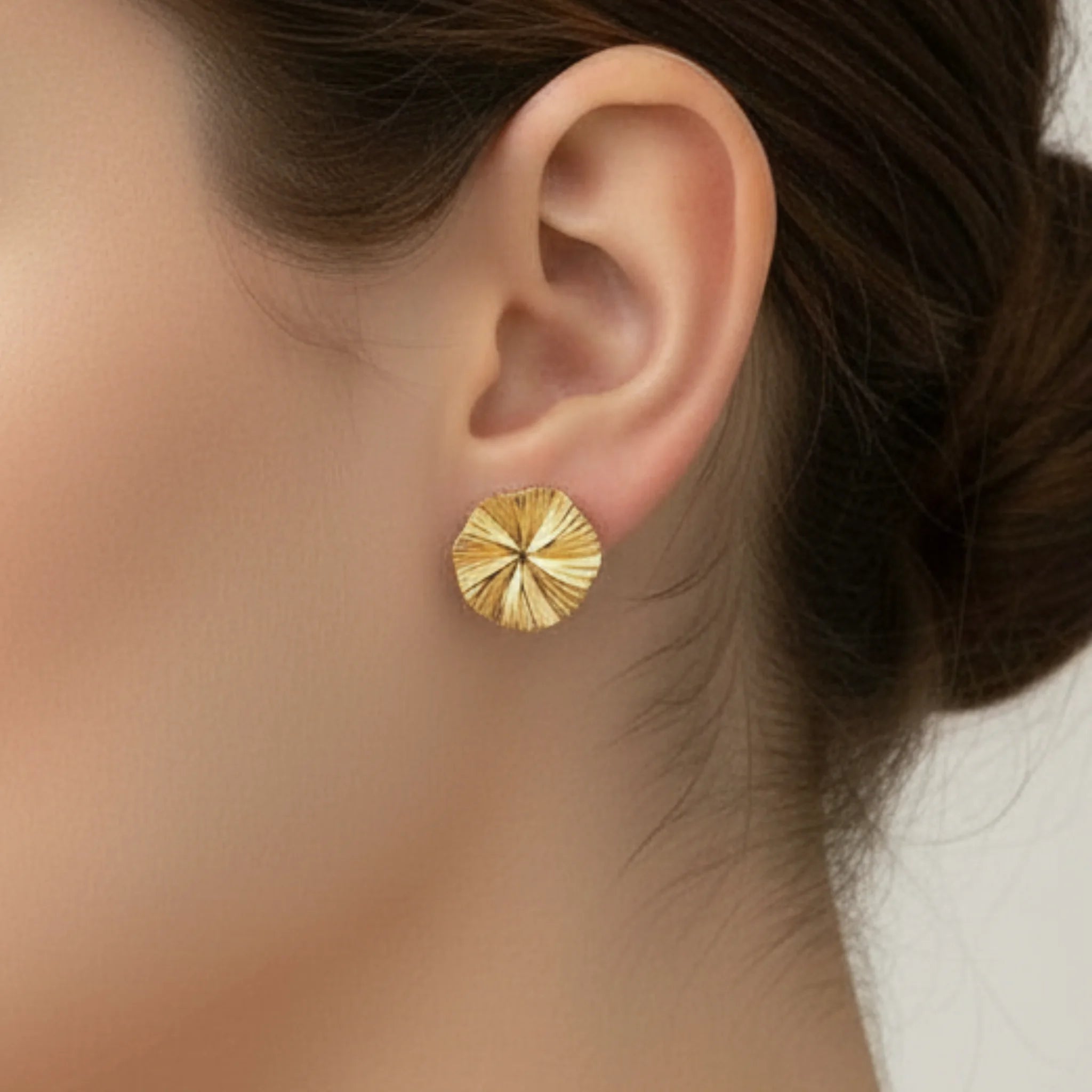 Gold textured bloom earring worn by a person with a blurred background