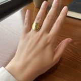 Hand wearing a gold textured disc ring on a wooden surface