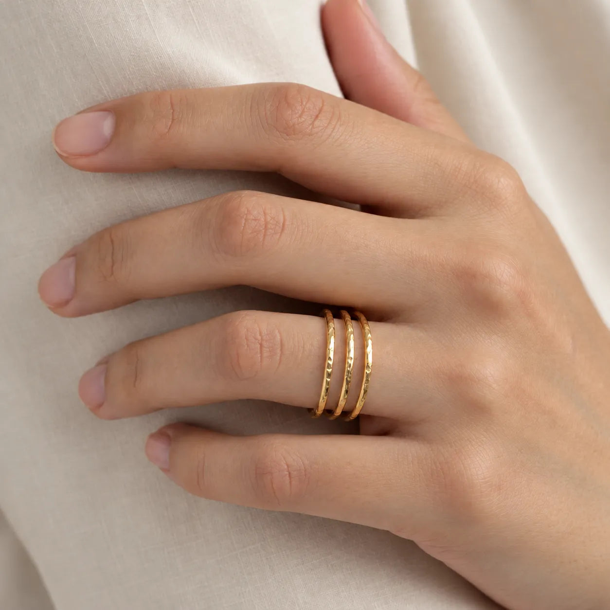 Hand wearing a textured triple band gold ring on a neutral background