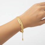 Gold triple herringbone chain bracelet on a wrist against a white background