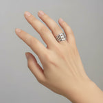 Hand wearing a silver triple layer ring on a plain background