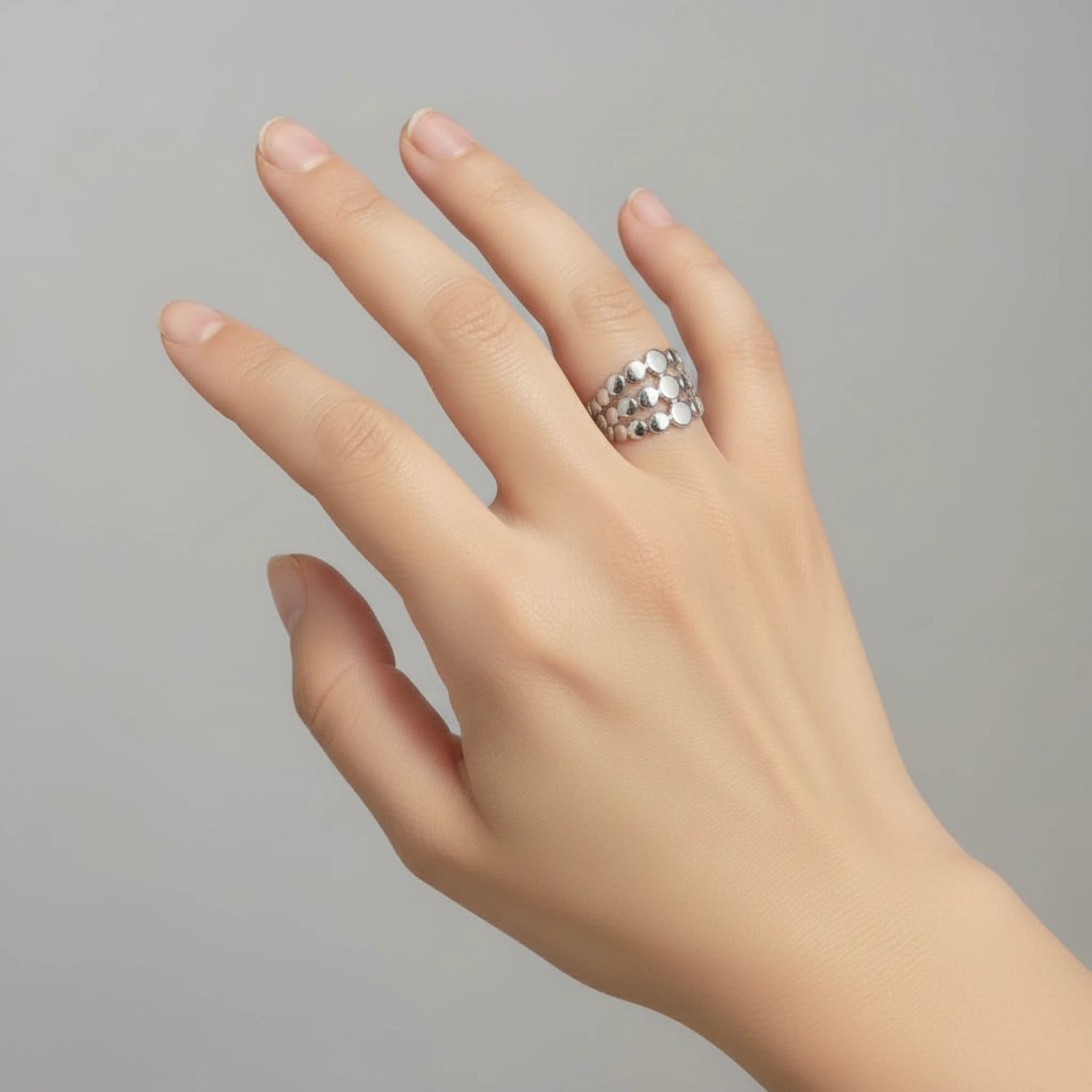 Hand wearing a silver triple layer ring on a plain background